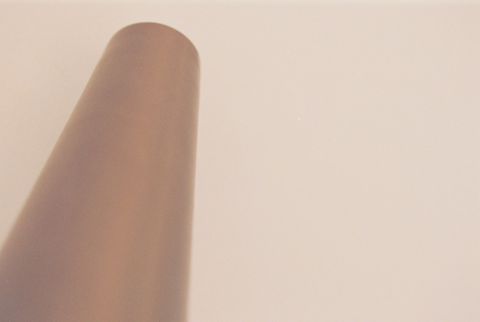 A soft cone-shaped shadow falling diagonally across a warm cream wall